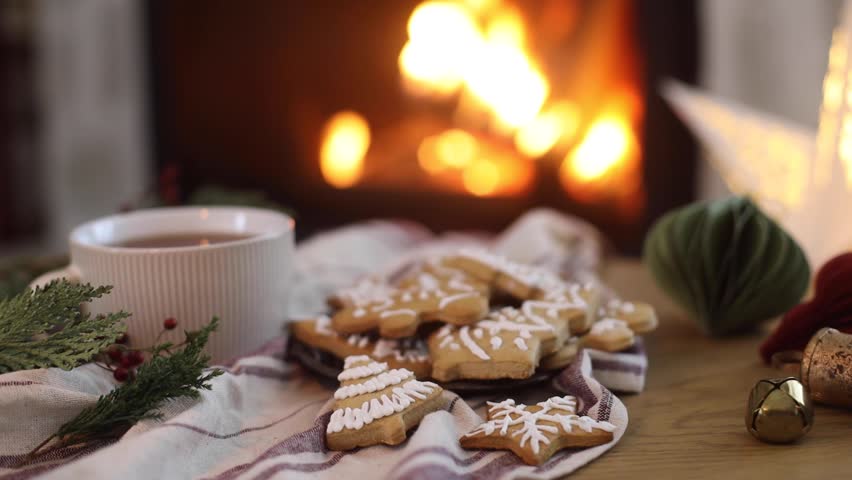 Gingerbread christmas cookies and warm cup of tea, fir branches and ornaments on table on background of burning fireplace. Cozy christmas video. Merry Christmas! 