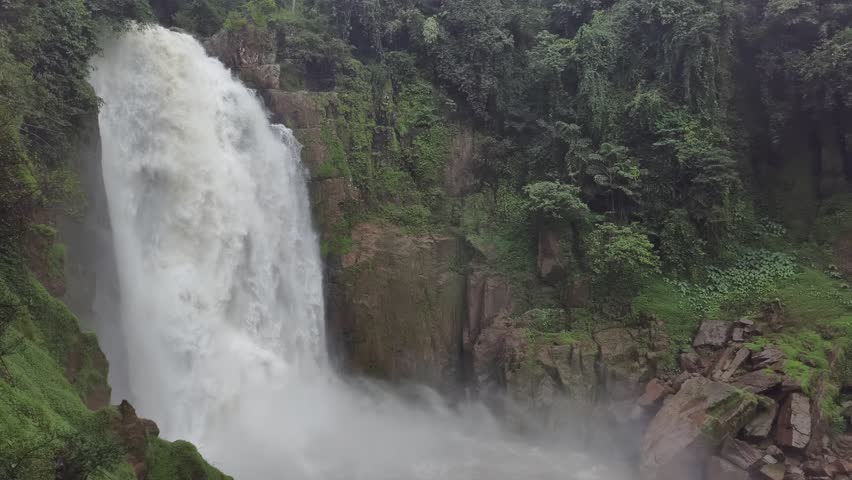 Ultra high‑definition 8K footage of a majestic waterfall cascading in a lush tropical forest. Mist rises around rock faces and dense greenery frames the scene. Ideal for cinematic nature, documentary.