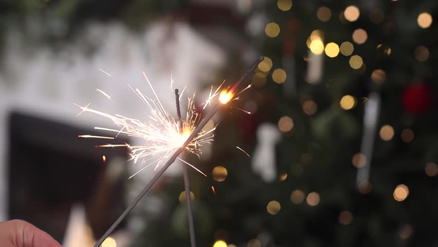Happy New Year video! Burning sparklers in hands close up on background of christmas tree golden lights. Glowing fireworks, new year eve holiday celebration