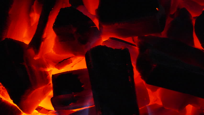 Charcoal, hot, glowing briquettes smoldering in a close-up shot of a barbecue grill with blue flames