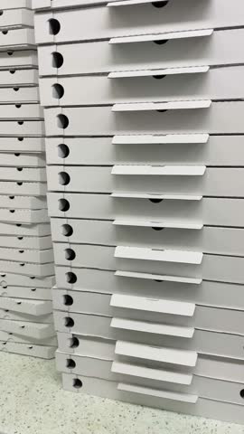 Vertical shot. Stack of cardboard pizza boxes placed together, showing food packaging material. Everyday food service packaging, reflecting fast food culture and takeaway practices.