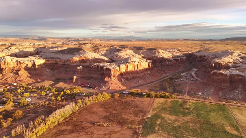 Aerial view of stunning sandstone cliffs reflecting warm sunlight, contrasting with the green fields below, near Bluff, Utah, United States.