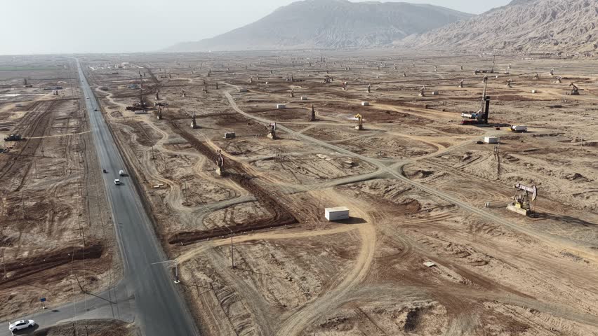Aerial view of pump jacks scattered across the arid landscape next to a road cutting through the desert, Turpan, China.