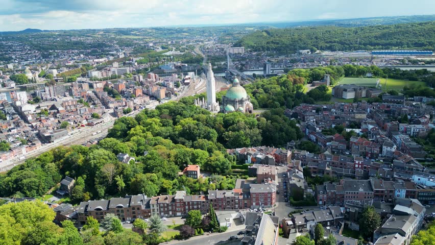 Aerial view of the Cointe Intermodal Terminal, a mix of urban buildings, green trees, and a prominent monument, Liège, Wallonia, Belgium.