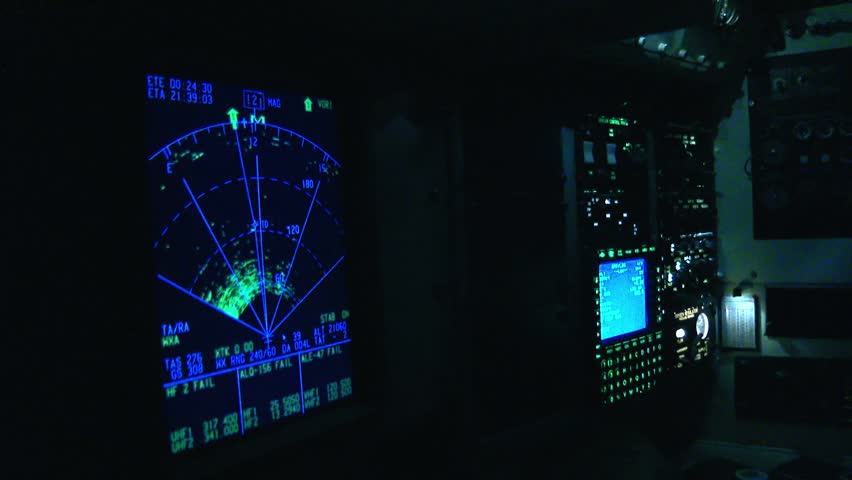 Flight deck instruments glowing in the dark as a pilot operates the complex avionics system. The radar display shows weather patterns ahead