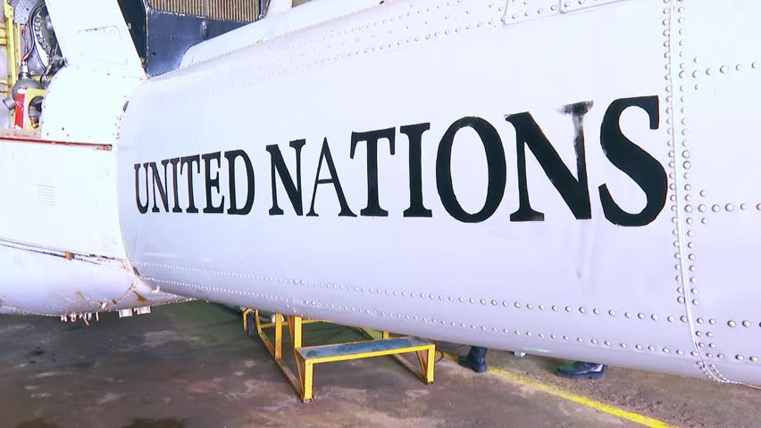 Close-up view of the united nations logo painted on the white fuselage of a helicopter tail boom parked inside an aviation maintenance hangar