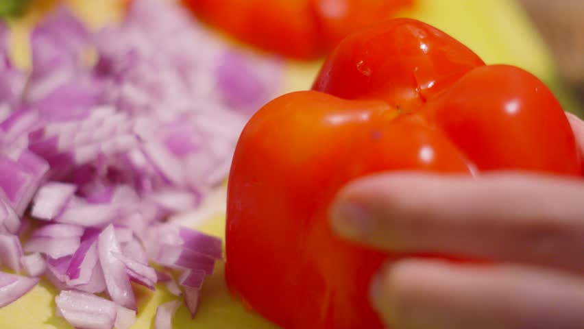 Close Up of Knife Chopping Peppers into Smaller Pieces with Finely Chopped Red Onions in Background.
