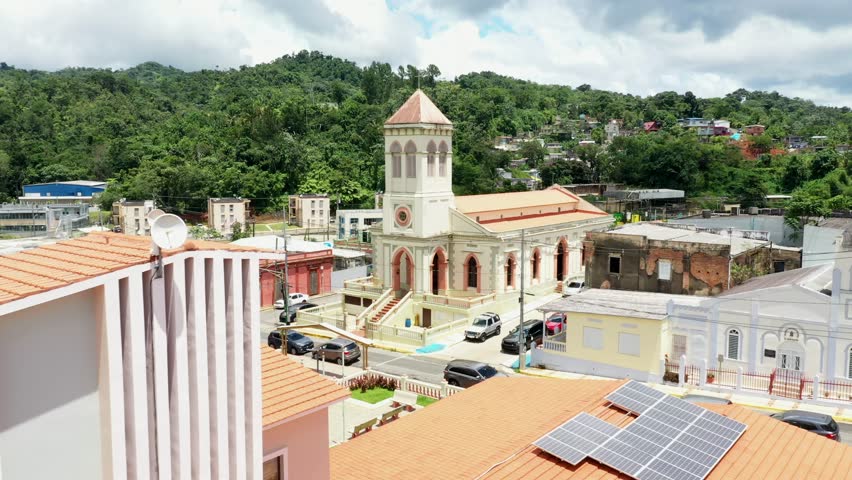 An aerial view of the historic Iglesia de San Juan Bautista with its iconic bell tower, surrounded by the colorful rooftops of the town of Maricao