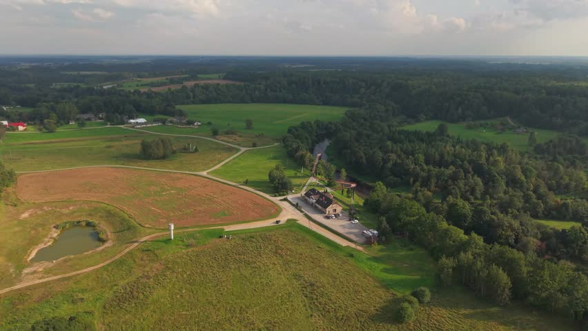 A drone view showcasing the lush rural landscape of Pagramantis, Lithuania, featuring an observation tower, forest, farmland, and buildings