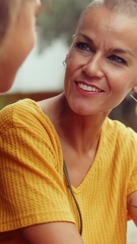 Vertical video, A young girl with long brown hair smiles at the camera. She is wearing a white top, gold necklace and has a shoulder bag.