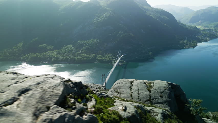Drone shot of the Lysefjord Bridge from the summit of Sokkaknuten in Norway in sunny weather. The sun is reflected in the water of the fjord.
