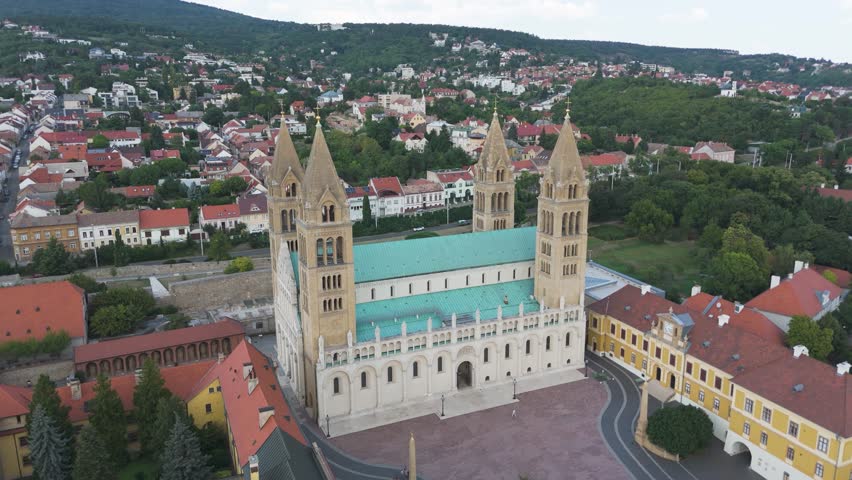 Drone orbiting Pécs Cathedral, highlighting its front facade, twin towers, and architectural details.