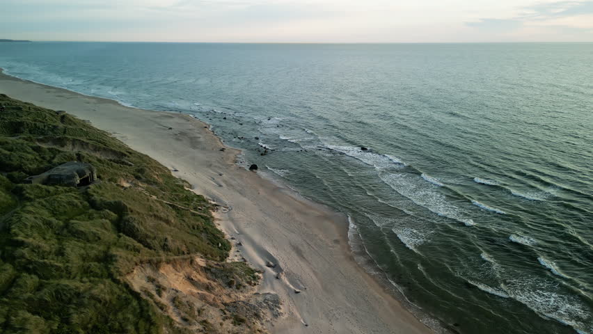 Evening drone flight with upward pan over the empty beach on the North Sea in Denmark. The sunset casts long shadows on the waves and dunes.
