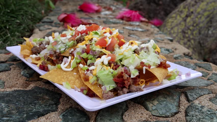 Loaded nachos topped with lettuce, tomato, cheese, and sour cream served outdoors on rustic surface