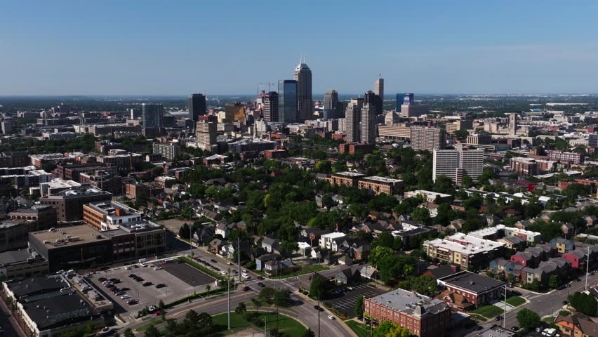 Drone moves backward over highway interchange revealing downtown Indianapolis skyline on summer day.
