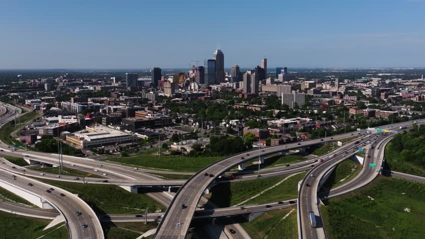 Drone moves forward over highway interchange toward downtown Indianapolis skyline on summer day.