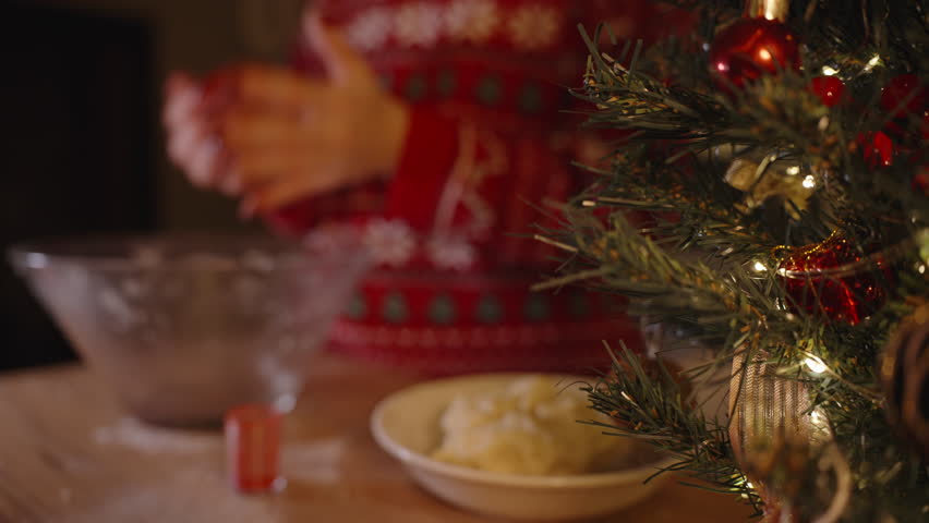 Woman Rolling Red Dough in Hands While Standing Next to Tree and Bowl of Yellow Dough on Flour-Dusted Table.