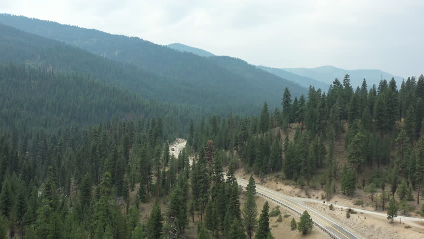 Aerial view of vehicles driving along the Ponderosa Pine Scenic Byway through Idaho’s forested Sawtooth Mountains on a hazy summer day beside the South Fork Payette River.