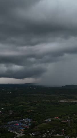 Vertical aerial view of Massive storm cloud releases rain over forested valley during tropical monsoon season
