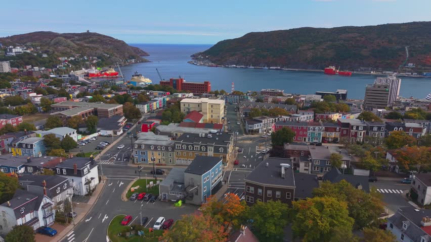 An elevated aerial glide over St. Johns, Newfoundland captures colourful row houses clinging to a hillside above the harbour amid vibrant fall foliage and crisp Atlantic air.