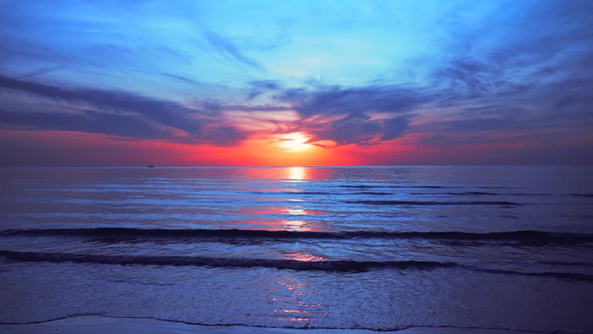 Romantic tropical sunset with blue and red magical sky over calm sea waves on the beach sand