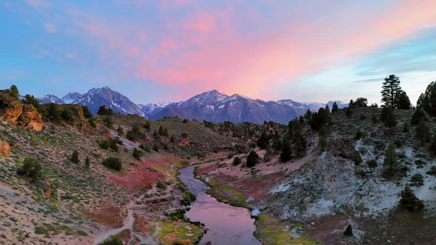 Aerial view backwards over a river in Hot Creek Geological Site, dusk in CA, USA