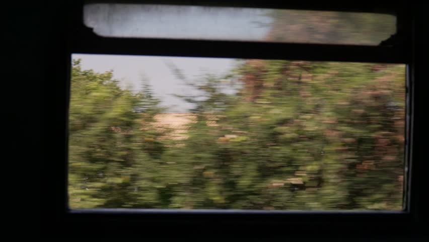 Train journey through lush green landscape seen from the window with a glimpse of a building