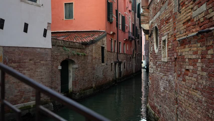 Narrow Venetian canal with brick houses and reflections