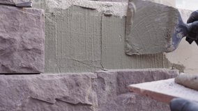 Close-up of masonry work as a construction worker demonstrates how to apply mortar to a wall before installing decorative stone. Hands in gloves preparing the surface during facade renovatio, training - Powered by Shutterstock - Get 15% off with code: PIKWIZARD15