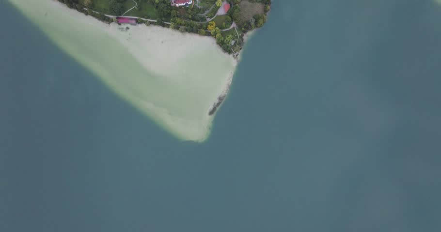 Aerial view of buildings and green trees contrasting with the blue waters of a lake, with light beige sandbanks, Fussen, Bavaria, Germany.
