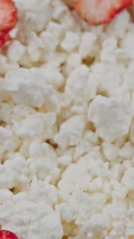 Vertical close-up of fresh cottage cheese topped with a spoonful of sour cream and strawberries. Healthy breakfast or dessert made with protein, seasonal fruit. Probiotic cold fermented kefir, yogurt