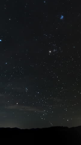 Starry night sky over mountain horizon, Bright constellations sparkle above dark mountains under the clear night sky, time lapse, vertical footage