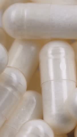 VERTICAL VIDEO: Rotating macro shot of white capsules, dietary supplements. Pharmaceutical production. Concept of medicine and healthcare, treatment, prevention, and wellness. Pills and vitamins macro