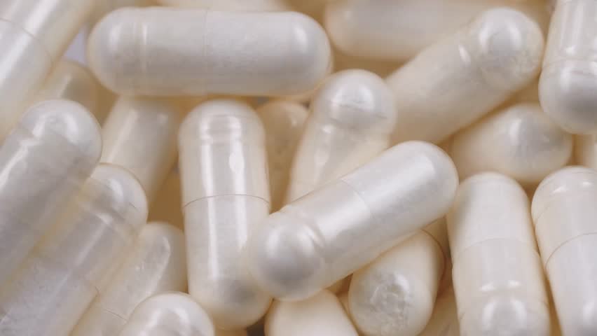 Rotating macro shot of white capsules, dietary supplements. Pharmaceutical production. Concept of medicine and healthcare, treatment, prevention, and wellness. Pills and vitamins macro.
