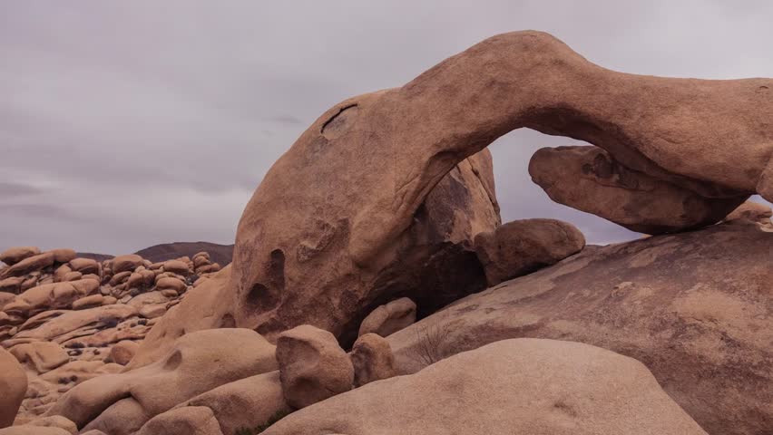 Scenic view of a natural arch in Joshua Tree National Park, showcasing rugged rock formations, desert landscape, and the park’s iconic geological features.
