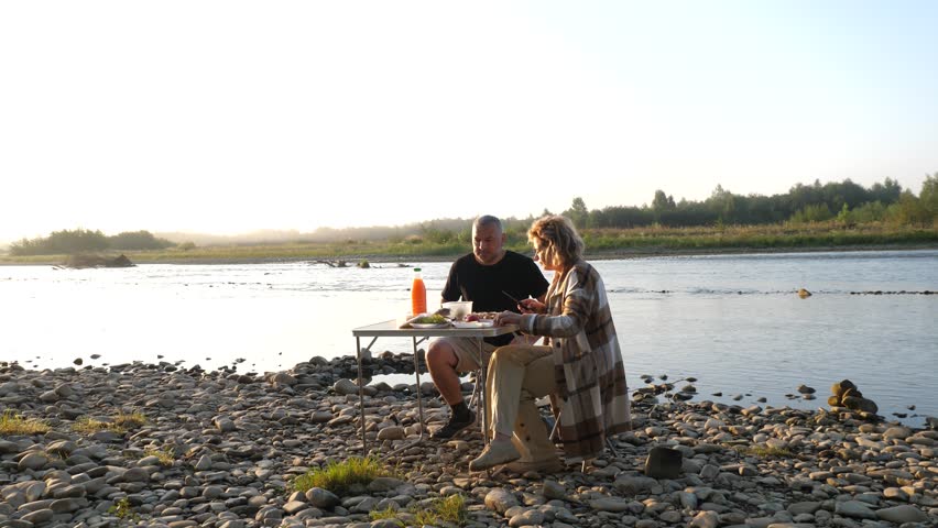 A man and woman had a picnic on the riverbank, enjoying food and drinks.