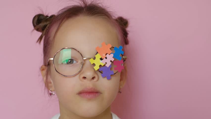 A child wearing eyeglasses with colored puzzle pieces decorated with a lens blows a kiss. Support for children with autism - Powered by Shutterstock - Get 15% off with code: PIKWIZARD15