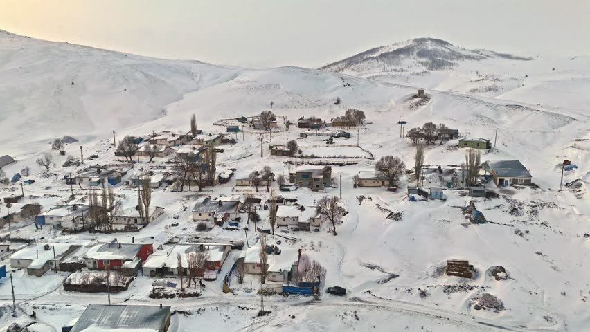 Aerial view of a snowy village with houses spread across the hills, hay bales, and roads. The calm beauty of winter and quiet rhythm of countryside life.