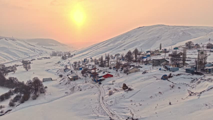 Aerial view of a snowy village with roofs, hay bales, and winding roads. Houses spread across the hills and the calm beauty of rural winter life.