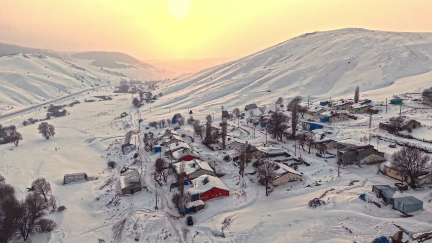 Aerial view of a snowy village with roofs, hay bales, and winding roads. Houses spread across the hills and the calm beauty of rural winter life.