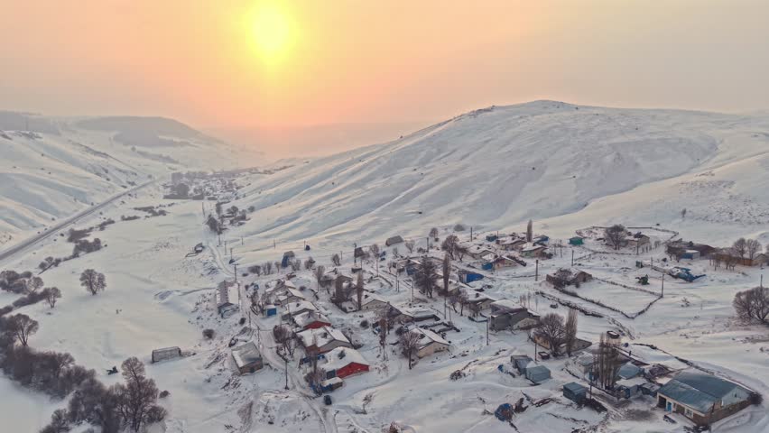 Aerial view of a snowy village with roofs, hay bales, and winding roads. Houses spread across the hills and the calm beauty of rural winter life.