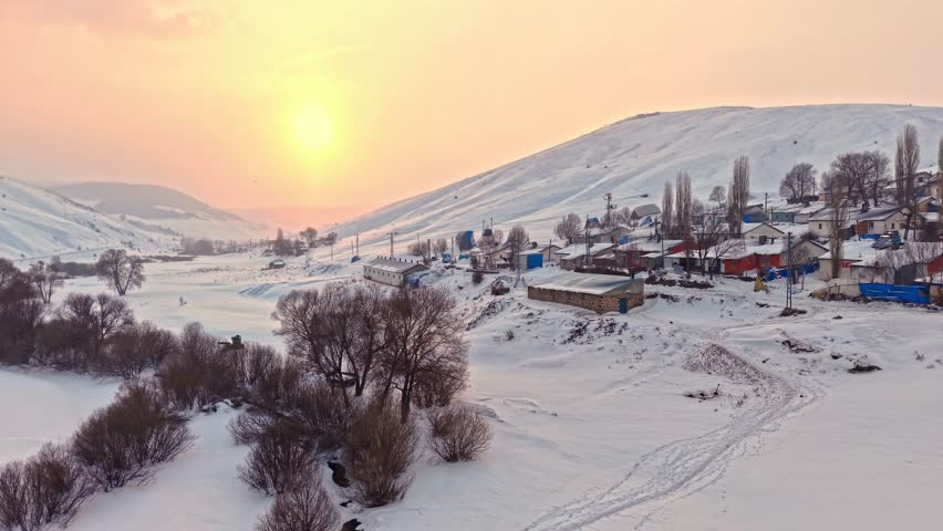 Aerial view of a snowy village with roofs, hay bales, and winding roads. Houses spread across the hills and the calm beauty of rural winter life.