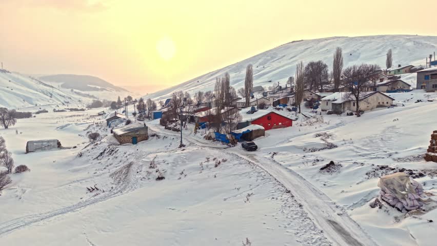 Aerial view of a snowy village with roofs, hay bales, and winding roads. Houses spread across the hills and the calm beauty of rural winter life.