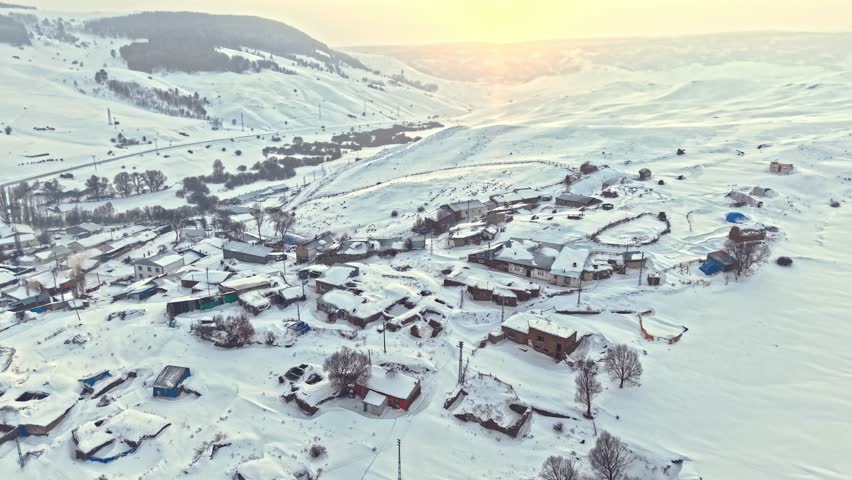 Aerial view of a snowy valley with a village and a winding road under soft daylight. Peaceful countryside and calm winter atmosphere.