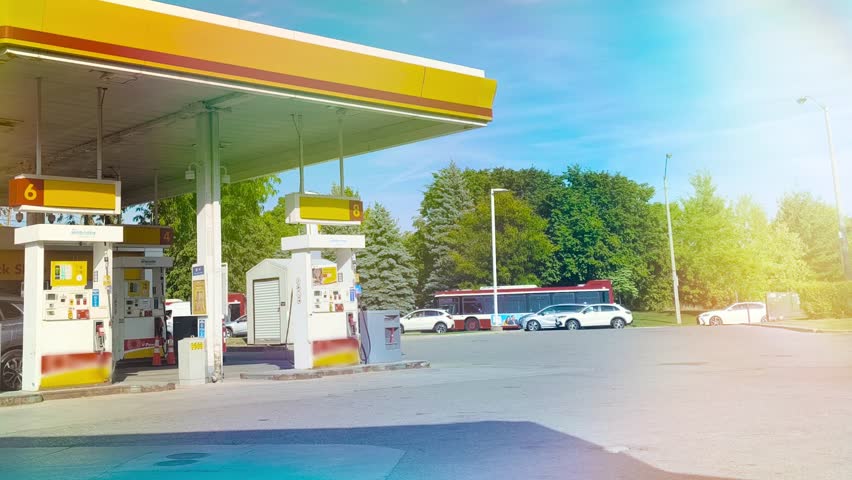Cars and a bus line up at a sunny gas station for refueling on a bright day, showcasing modern transportation and energy infrastructure against a backdrop of lush greenery and clear skies