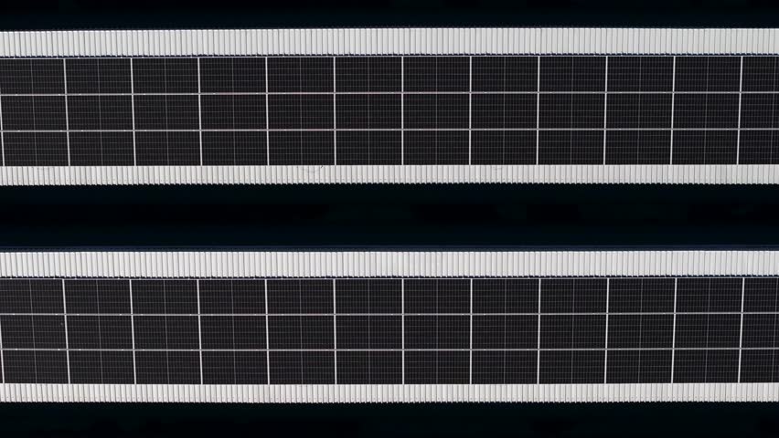 Moving above solar panel power plant on roof of a company building, aerial view. Rooftop PV modules for renewable energy generation, drone shot