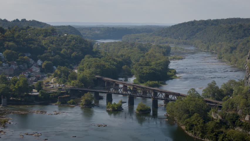 View from Split Rock Overlook showing historic Harpers Ferry and the confluence of the Potomac and Shenandoah Rivers, framed by forested hills and an old railway bridge.