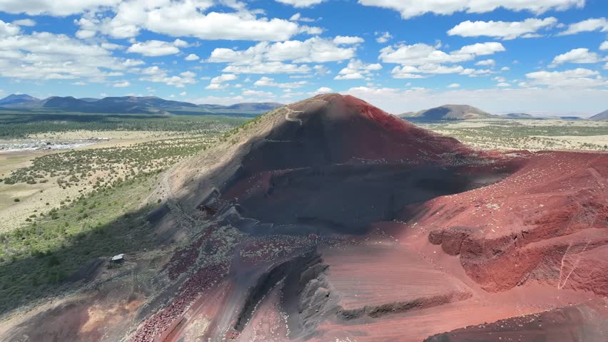 Aerial view of a reddish-black volcanic cinder cone, Cinder Mountain, casting shadows on the arid landscape, with scattered vegetation, Flagstaff, Arizona, United States.