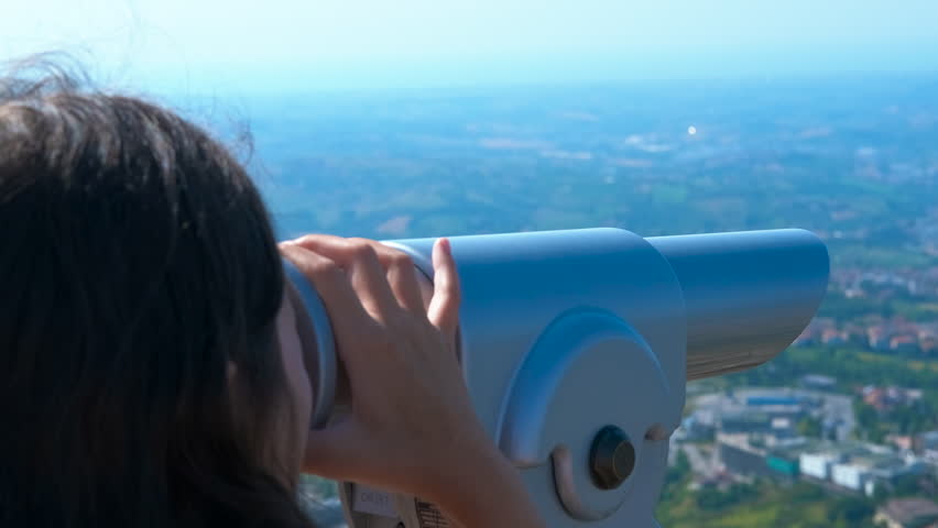 Tourist observing cityscape through telescope. Young woman gazing through telescope, exploring urban landscape with curiosity and wonder, enjoying panoramic cityscape view on bright sunny summer day