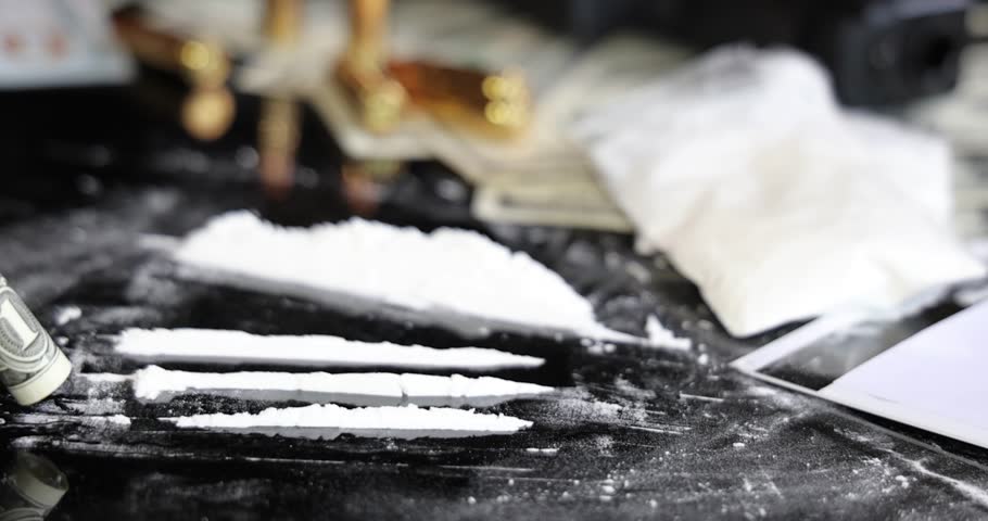 Snorting a line of cocaine with a rolled dollar bill on black background, slow motion. Illegal drugs and cash with gun and bullets on table - crime scene. Criminal problems. Illegal selling